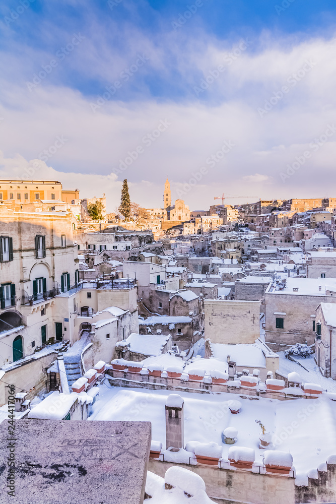 Fototapeta premium panoramic view of typical stones Sassi di Matera and church of Matera 2019 under blue sky with clouds and snow on the house, concept of travel and christmas holiday, capital of europe culture 2019