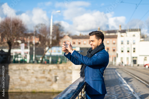 Handsome business man taking a picture with mobile phone outdoors.