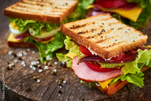Fototapeta Naklejka Na Ścianę i Meble -  Homemade sandwich with ham, lettuce, cheese and tomato on a wooden background
