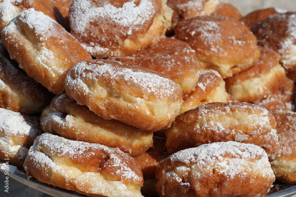 Fried custard donuts sprinkled with powdered sugar, stacked on top of each other on the tray. Closeup