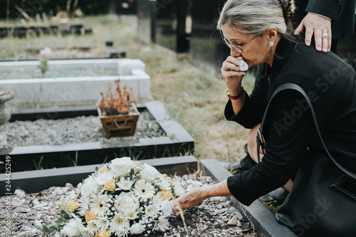 Canvas Print Old woman laying flowers on a grave