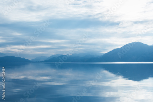 Mountains silhouetted against clouds and mist with sky reflection on calm lake