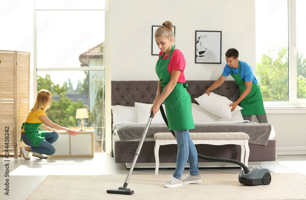 Team of professional janitors in uniform cleaning bedroom