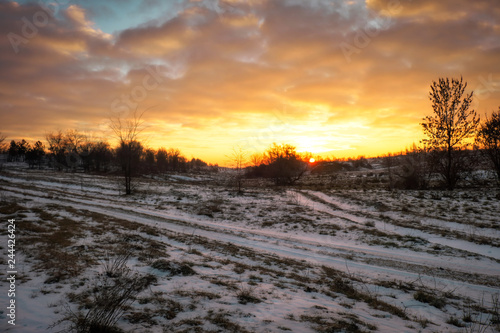 Dirt track through a field of snow at dawn or dusk. A Snow-covered country road through the fields at sunset.