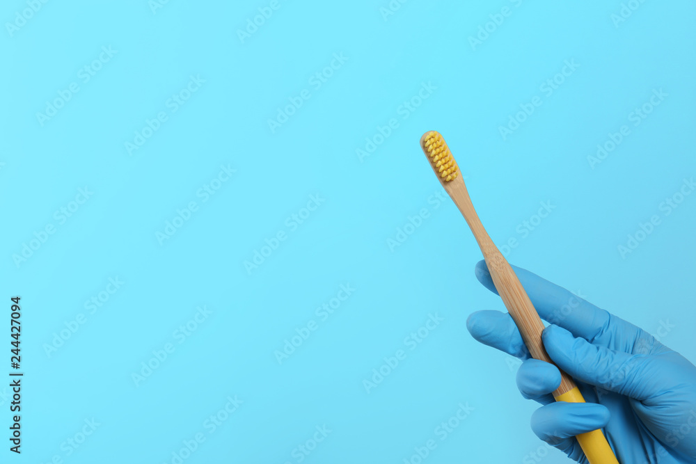 Dentist holding wooden toothbrush on color background, space for text