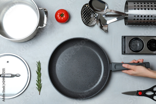 Woman holding frying pan over table with clean cookware, top view photo