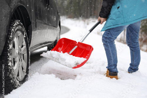 Man cleaning snow with shovel near stuck car outdoors
