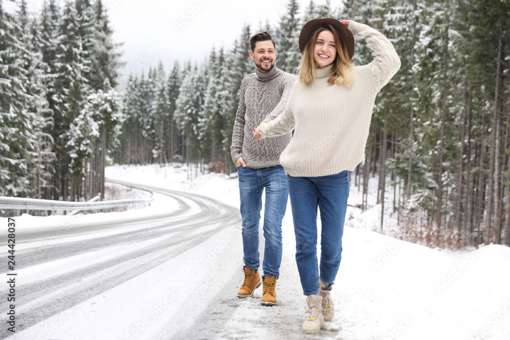 Couple walking near snowy forest, space for text. Winter vacation