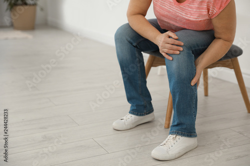 Mature woman suffering from leg pain at home, closeup. Space for text