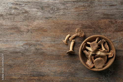Bowl of dried mushrooms on wooden background, top view with space for text