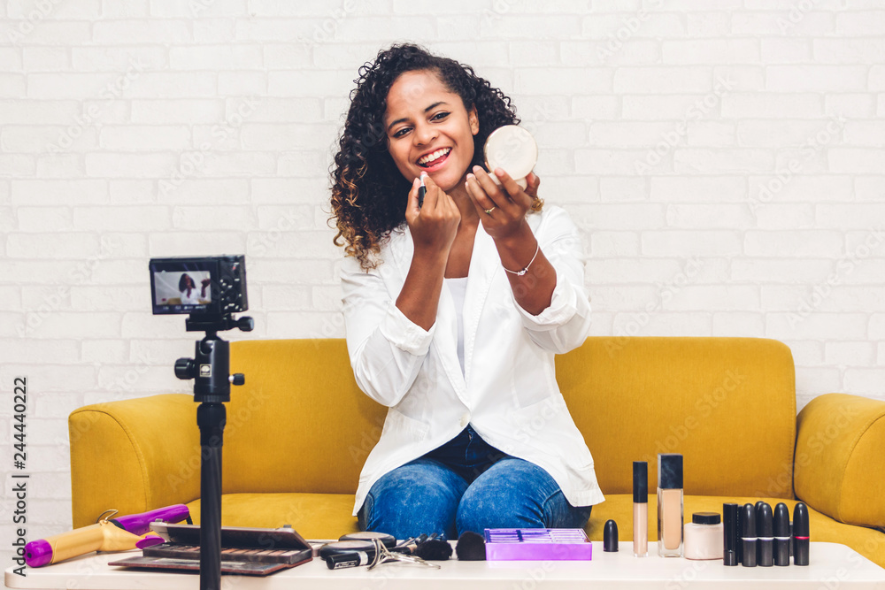 African american woman blogger in front of camera recording vlog herself talking about with makeup cosmetics for internet social networks at home