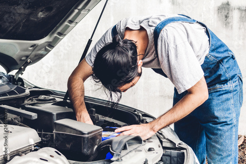 Professional car mechanic in uniform  fixing a car engine and repairing checking under the car hood in auto service