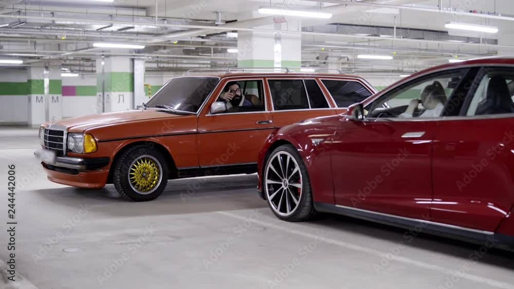 Young female with ponytail sits in red car putting her head on steering wheel when other car with mature male driver stops nearby in underground garage. Young female with ponytail sits in red car putting her head on steering wheel when other car with mature male driver stops nearby in underground garage.