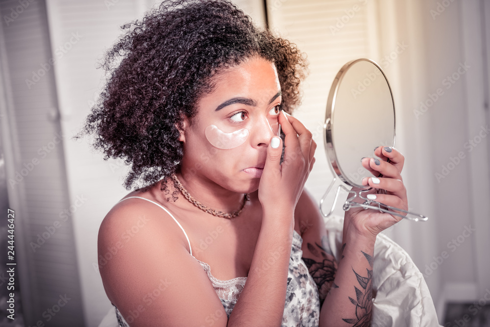 Focused short-haired woman wearing eye lenses while looking in the mirror Focused short-haired woman wearing eye lenses while looking in the mirror