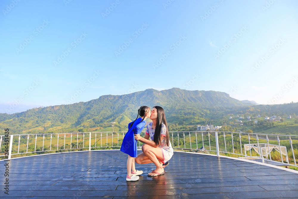 Asian mother and daughter kissing on balcony at hillside.