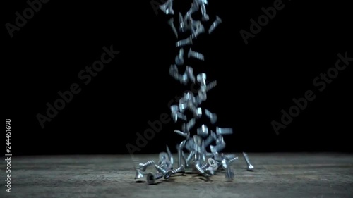 Slow motion of falling screws on wooden table on black background.