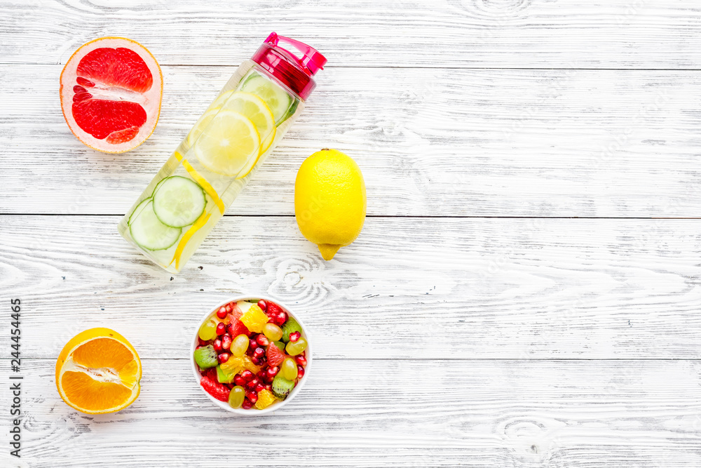 Diet rich in fruits. Slimming diet. Fruit salad near fruit lemon and cucumber water on white wooden background top view copy space Diet rich in fruits. Slimming diet. Fruit salad near fruit lemon and cucumber water on white wooden background top view copy space