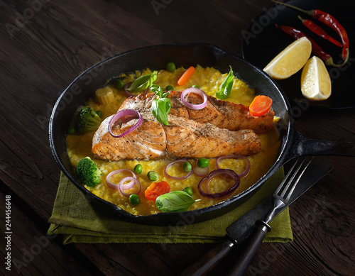 baked salmon steak  in a pan on a corn palette with basil on a wooden background. rustic style.