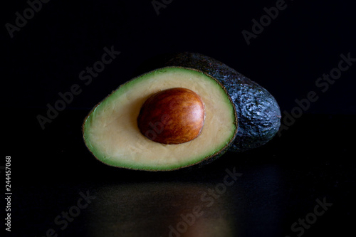Whole and halved avocado on black lit by natural light