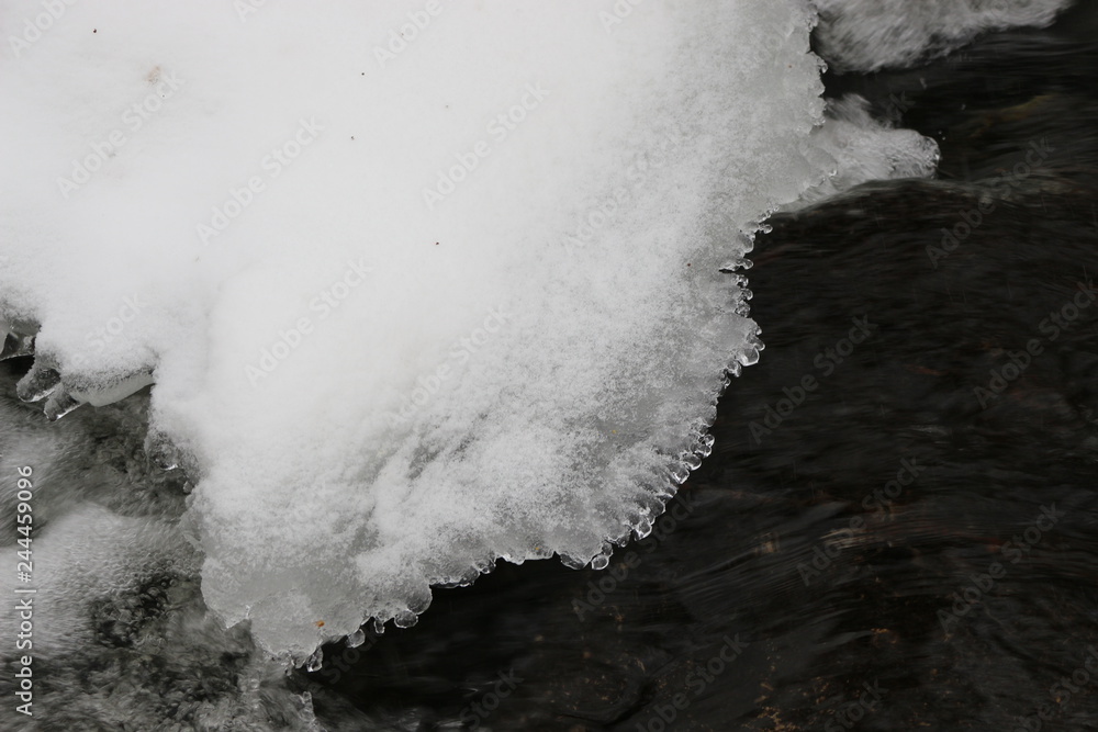  Frozen snow hangs over flowing water.