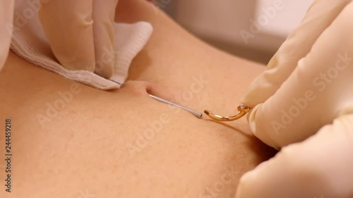 closeup slow motion master inserts beautiful belly button ring into beveled-tip hollow medical needle for piercing 