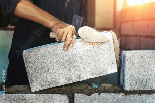 Fototapeta Worker building wall bricks with cement