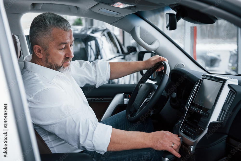 Buying and testing new automobile. Senior businessman in official clothes sits in a luxury car and pushing the buttons on the music player Buying and testing new automobile. Senior businessman in official clothes sits in a luxury car and pushing the buttons on the music player