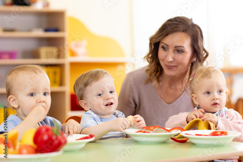Babies and kindergartener together eat fruits and vegetables as a snack in the kindergarten, nursery or daycare