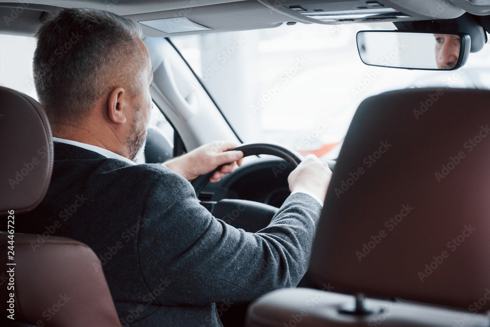 Going to the meeting. View from behind of senior businessman in official clothes driving a modern new car Going to the meeting. View from behind of senior businessman in official clothes driving a modern new car