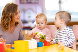Nursery babies playing toys with teacher in playroom at preschool or kindergarten. Education concept.