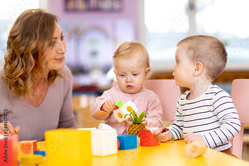 Nursery babies playing toys with teacher in playroom at preschool or kindergarten. Education concept.