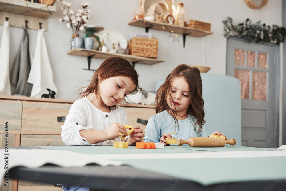 Leisure time when parents is not at home. Two kids playing with yellow and orange toys in the white kitchen Leisure time when parents is not at home. Two kids playing with yellow and orange toys in the white kitchen