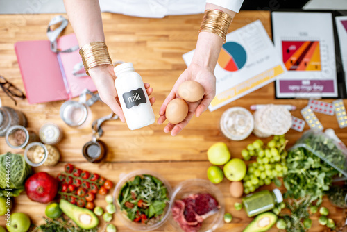 Dietitian holding milk and eggs above the table full of various healthy products and drawings on the topic of healthy eating photo