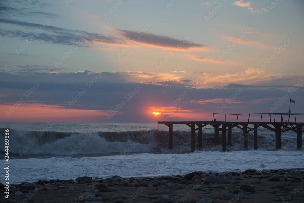 sun setting over Batumi beach Dock, as powerful waves roll in, and a very colorful sky is reflected on the beach