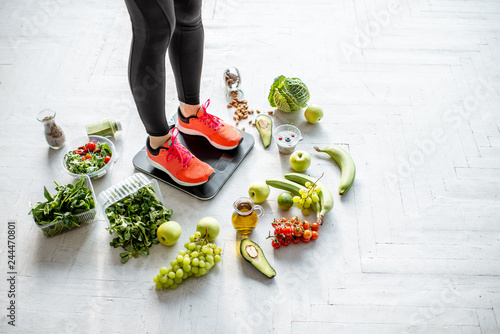 Tablou pe pânză Sports woman weighing on the scales with healthy food around