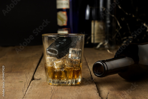 Car keys in a glass with an alcoholic drink and an empty bottle on a wooden background. Drunk driving concept, stop drinking and driving.
