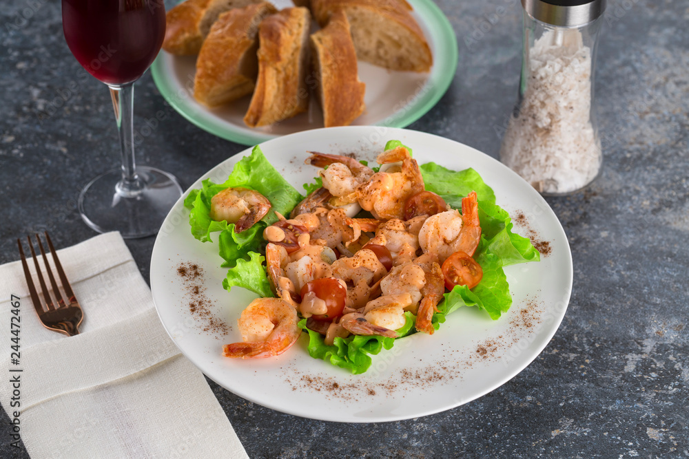 salad with Royal prawns on a white plate on the dark surface of the table with Cutlery.