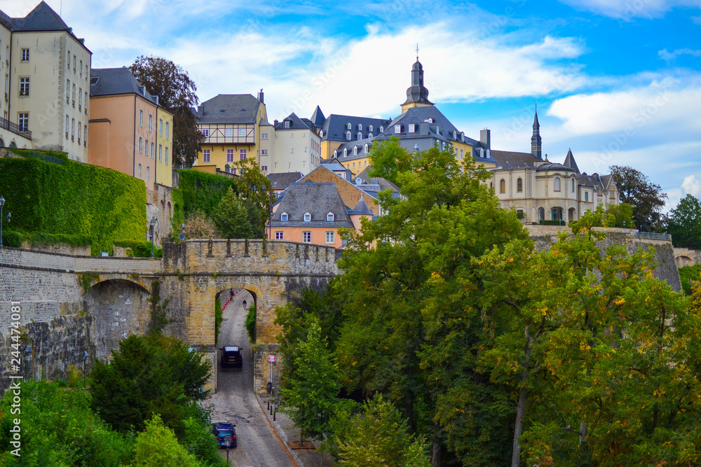 View of a medieval gate or door in the wall of the old town of Luxembourg, Europe, with buildings and church at the background and trees at the foreground