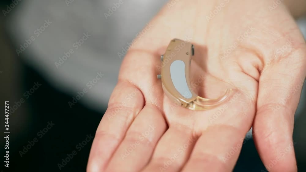 The hearing aid lies in the female palm. The hearing aid lies in the female palm.