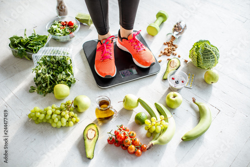 Foto Sports woman weighing on the scales with healthy food around