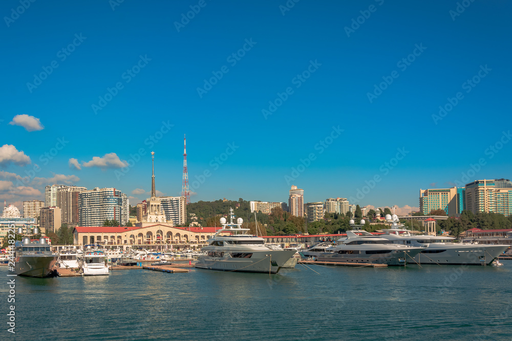 Sea port in summer. Many different yachts and boats stand at the marina. Yachtsmen and travelers are preparing to sail in the sea. In the background of the building of the seaside city.