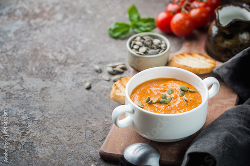 Healthy tomato soup in a white bowl with cream and pumpkin seeds
