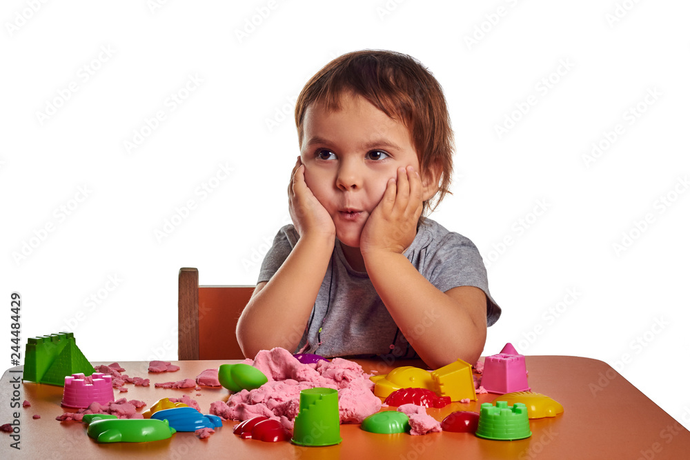 Emotional little child girl playing with kinetic sand on the orange table. Isolated white background Emotional little child girl playing with kinetic sand on the orange table. Isolated white background