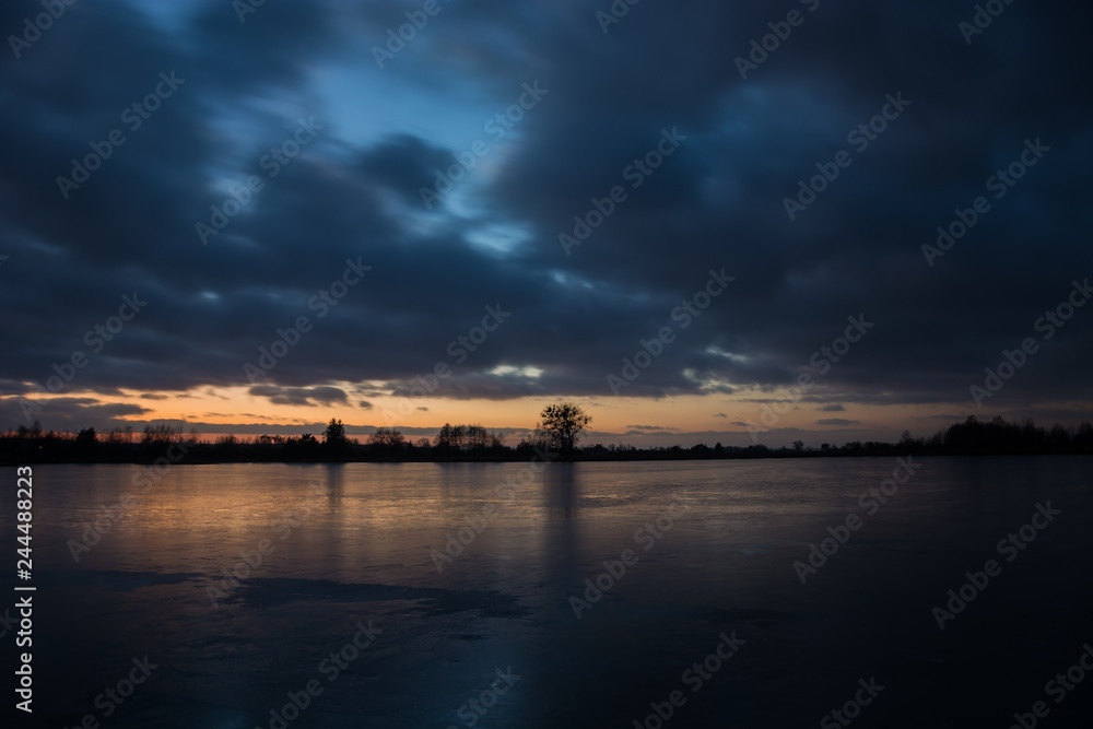 Cloudy dark sky after sunset on a frozen lake and reflecting light on the ice