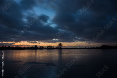 Cloudy dark sky after sunset on a frozen lake and reflecting light on the ice