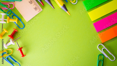 Stationery on green background. Pens, pencils, scissors, paper clips, color push pins and on the table. View from above with copy space