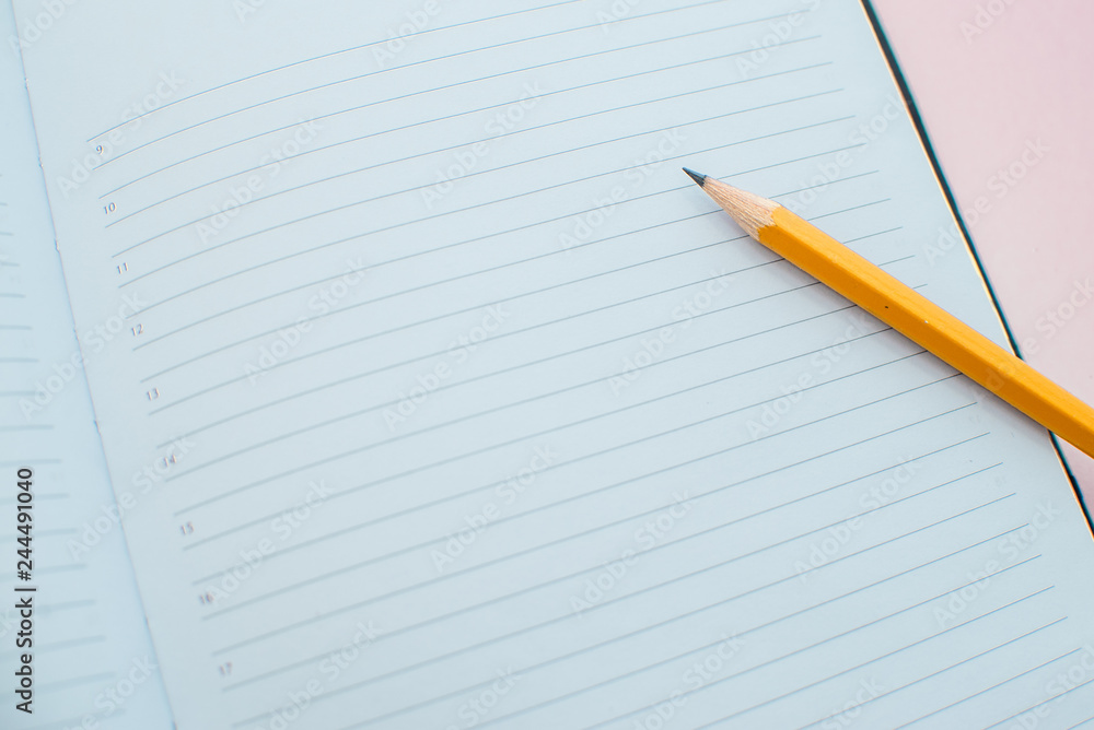 A pencil on a notebook in the linel. School supplies. White sketch book with orange pencil. Note book and pencil A pencil on a notebook in the linel. School supplies. White sketch book with orange pencil. Note book and pencil