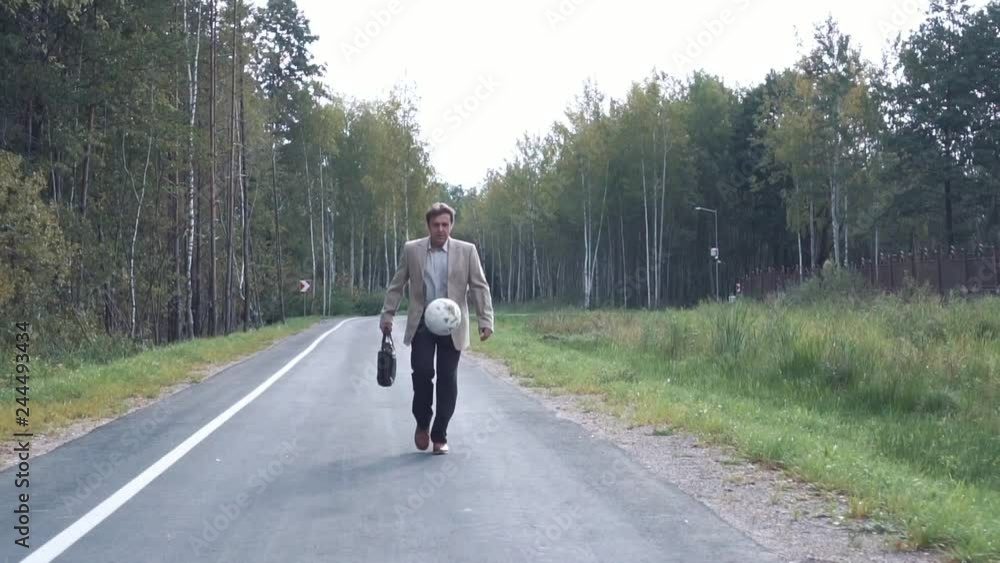 An elderly businessman in a business suit with a briefcase walking along the road next to the park, catching a soccer ball and playing with it An elderly businessman in a business suit with a briefcase walking along the road next to the park, catching a soccer ball and playing with it