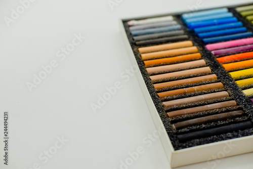 Close up view of bright colorful pastel chalks on white background. Set of multicolored pastel crayons in openartist box on a white background, top view.