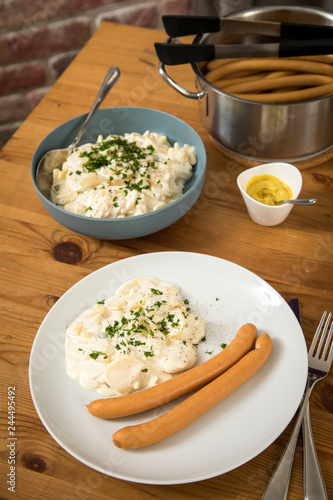 Wiener Würstchen im Topf, Senf und Norddeutscher Kartoffelsalat mit Mayonnaise, Ei und Gurke als Mahlzeit auf Holz Tisch